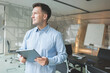 © muse studio - Professional man holding a tablet in a modern office conference room, looking away, contemplating