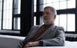 © opolja - Portrait of handsome bearded mature businessman looking away thoughtfully while sitting on sofa.