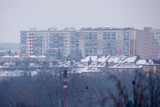 Zimowa panorama miasta (Ostrowiec Świętokrzyski) w mglisty, zimowy dzień. Panorama przedstawia mglisty dzień z dachami pokrytymi śniegiem. Na pierwszym planie widać bezlistne drzewa i komin