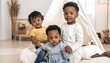 © Gun - Three adorable Black children pose together near a white tent in a bright room