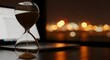 © MdShahid - Business Time Management: Hourglass on desk with laptop and bokeh city lights, deadline pressure, productivity and work life balance concept