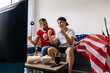© kleberpicui - American father and teenage son watching a sports game together, cheering and reacting during an exciting match at home.