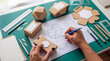 © SnapSpark Studios - Designer working on packaging prototypes and blueprints with drafting tools and craft supplies