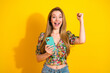 © deagreez - Happy young woman with phone celebrates in bright yellow studio wearing floral top and jeans