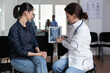 © DC Studio - Female medical specialist interpreting digital x ray in hospital waiting room. Doctor explaining young patient diagnosis in medical clinic. Woman listening explanation of sanatorium nurse.