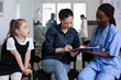 © DC Studio - African american doctor filling out child admission paperwork to pediatric hospital. Young woman hospitalizing sick daughter in medical clinic. Nurse attending mother, little girl in sanatorium lobby.