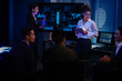 © ultramansk - Confident businesswoman presenting global data analysis to team on large digital screen. Professional executive leading IT strategy meeting in modern blue light night office.