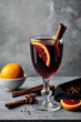 © Rayan Heaven - A glass of hot mulled wine garnished with orange slices and cinnamon sticks, surrounded by star anise and fresh citrus on a dark stone surface