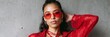 © Andrii Zastrozhnov - Female mixed adult model wearing red sunglasses and red sheer blouse posing against concrete wall fashion portrait