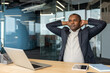 © Liubomir - Mature businessman sitting at an office desk, stretching his arms behind his head, taking a moment to relax and clear his mind during a busy workday in a modern corporate environment