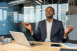 © Liubomir - Mature man in a suit meditating at his office desk with eyes closed and hands in a mudra gesture, finding calm and focus amidst the contemporary workspace