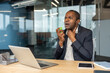 © Liubomir - Man in suit at office desk holding his throat and using oral spray for sore throat while working on laptop, managing illness and seeking quick relief during workday