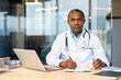 © Liubomir - Professional african american doctor sitting at desk, reviewing patient records and holding medication, providing expert healthcare service in a modern medical setting