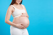 © New Africa - Pregnant woman touching her belly on light blue background, closeup. Space for text