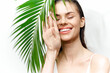 © VICHIZH - Young woman with a bright smile hiding behind a palm leaf, showcasing natural beauty and tropical vibes. Perfect for lifestyle and wellness themes.