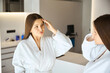 © Svitlana - Beautiful woman in white bathrobe looking at mirror posing in beauty salon