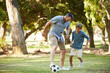 © peopleimages.com - Father, boy and play with football at park for bonding, exercise and fun with teaching, kick and outdoor in summer. People, dad and child with love for soccer, pass or dribble with learning on grass