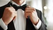 © dmmarychev - Close up of man hands adjusting black bow tie on white shirt and tuxedo