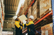© ฺฺฺBoonterm - Two male warehouse workers are helping each other lift heavy cardboard boxes onto shelves. The two workers support each other to complete the task : Two workers are carrying the boxes manually without