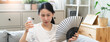 © Pormezz - Suffering summer heat wave stroke, hot weather, tired asian young woman feeling discomfort sweaty, sitting on couch in living room, hand fan in blowing, wave fan to ventilation when high temperature.
