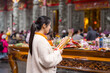 © leungchopan - Female visitor offering incense in peaceful temple