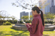 © leungchopan - Woman using phone outdoors in sunny park setting