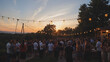 © Stacy - A beautiful outdoor gathering at sunset with people socializing under string lights, creating a warm and inviting atmosphere.