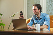 © Teodor Lazarev - Smiling man multitasking with laptop and smartphone at home