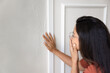 © fizkes - Close-up view of concerned, shocked young woman wearing glasses touching damaged interior wall with visible cracks or water stains. Home maintenance issues, property inspection, and renovation needs