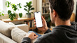 © MD Rashedul Islam - Hand holding mobile smartphone blank screen mockup cozy sofa lifestyle, man relaxing on couch using phone for social media app, digital technology home copy space advertising