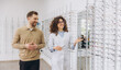 © anatoliycherkas - Optician helping customer choosing new eyewear frames in a modern ophthalmology clinic, selecting eyeglasses for improved vision
