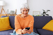 © Xavier Lorenzo - Happy senior woman enjoying winter day at home while entertaining using mobile phone, reading some news or watching social media content on app. Technology lifestyle concept.