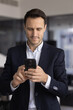 © fizkes - Confident adult man corporate manager executive messaging on cellphone in work office making online payment via mobile banking app managing digital document in corporate network reading business news