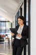 © David - In a chic and inviting office, a professional woman engages with her tablet, embodying modern elegance and the evolution of digital communication in the workplace.