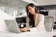 © fizkes - Positive businesswoman sits at desk working on laptop, lead pleasant business chat, review report with smile, feel satisfied with workflow in modern workplace. Business communication, innovative tech