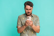 © Andrii Iemelianenko - Middle-aged man anxiously types fast on smartphone, breathing deeply while focused on composing urgent message. Young adult guy on blue background shows tension, nervousness, digital communication.