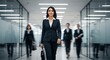 © Fatin - A confident businesswoman in a sharp suit leads a team down a modern office hallway.