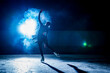 © kinomaster - Silhouette of a figure skater performing on a dark indoor ice rink with bright blue backlight and mist. Dramatic winter sports scene with elegant pose, motion and theatrical atmosphere.
