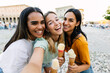 © Xavier Lorenzo - Three young diverse women enjoying an ice cream while taking selfie during their summer vacation in a European tourist city. Happy female friends celebrating friendship on a sunny day