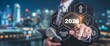 © Tusher - Visionary's Gaze: A business figure, poised in a sharp suit, interfaces with a futuristic digital interface, foreseeing the pivotal year 2026 amid a backdrop of a city skyline.