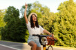 © Home-stock - Happy woman riding electric bicycle on bike path in city green park outdoors, singing song and raising one hand. Active lifestyle concept