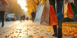 © miss irine - Woman walks with shopping bags on city street covered with autumn leaves. Sunlight shines through trees on a pleasant fall day. People enjoy outdoor retail and seasonal leisure.