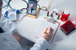 © Floren Horcajo - Doctor writing notes on clipboard, engaging in telemedicine, surrounded by medical supplies and blood samples