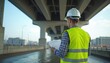 © Vadym - Engineer in hard hat and hi-vis vest examines documents under large overpass bridge. He checks structural details and inspections. Man works on infrastructure project. Urban construction planning.