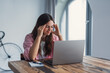 © Daniel - Tired woman massaging temples, suffering from headache after computer work, sitting at desk with laptop at home, exhausted young female with closed eyes touching head, relieving pain, migraine