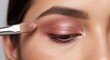 © Von - A makeup artist applies eyeshadow to a woman's eye. She uses a brush to blend a shimmering, warm-toned eyeshadow onto her eyelid.