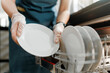 © Konstantin Yuganov - Hands in Protective Gloves Loading Clean Plates into Dishwasher in Commercial Kitchen