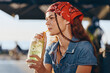 © SHOTPRIME STUDIO - Young woman with red bandana drinking a refreshing cold beverage outdoors in warm sunlight, casual style and relaxed mood in summer setting.