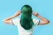 © Pixel-Shot - Young woman with green hair in headphones on blue background, back view