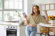 © Pixel-Shot - Cool young woman with mobile phone listening to music and dancing in kitchen